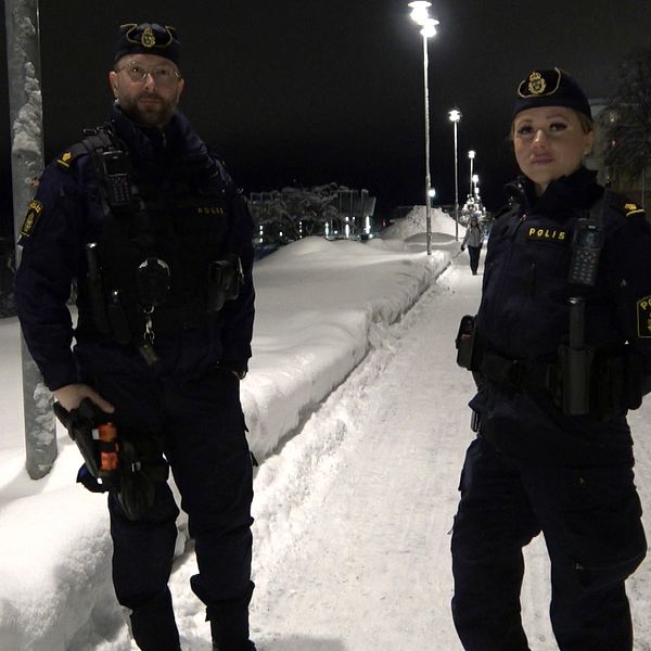 två poliser i unifrom på en snöig gågata upplyst av gatlampor