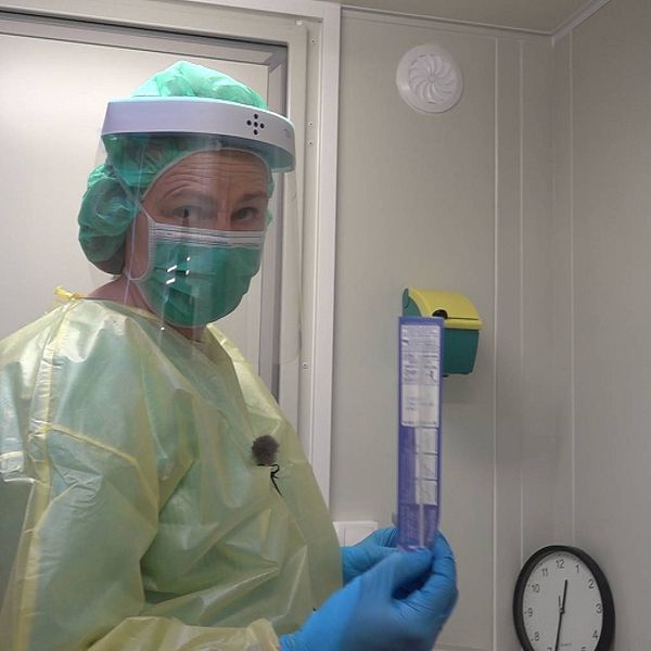 Kvinna i full skyddsmundering håller i en testpinne för covid-test.