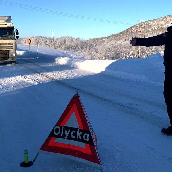 Polis står och visar in en lastbil på en parkeringsyta. Vinter. En skylt med texten ”olycka” står på vägen.