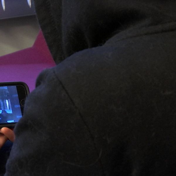 En kvinna med svart luvtröja tittar på ett klipp i en mobiltelefon.