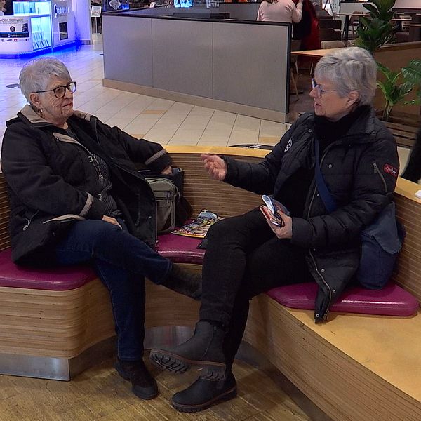 Lena och Rose-Marie Asplind sitter på en bänk i ett köpcentrum.