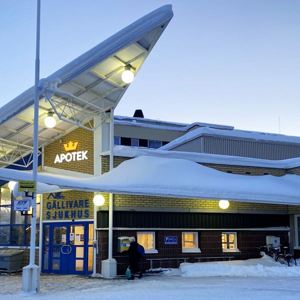 Stor byggnad i gult tegel med snö på taket. Ovanför dörren står det Gällivare sjukhus och Apotek.