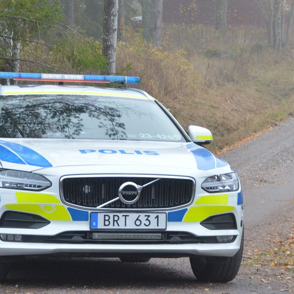 polisbild i förgrund, grusväg in mot fastighet med flera fordon