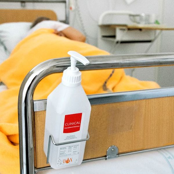 En flaska handsprit som fästs på en sjukhussäng där det ligger en patient.