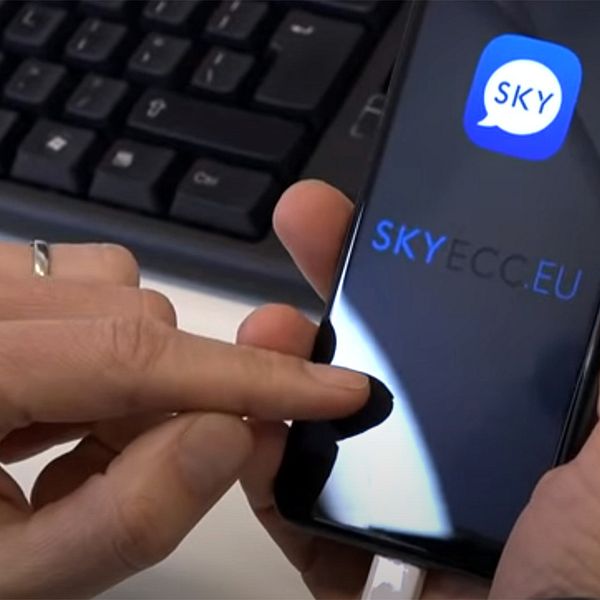 En polis sitter med en smartphone och öppnar appen Sky ECC.