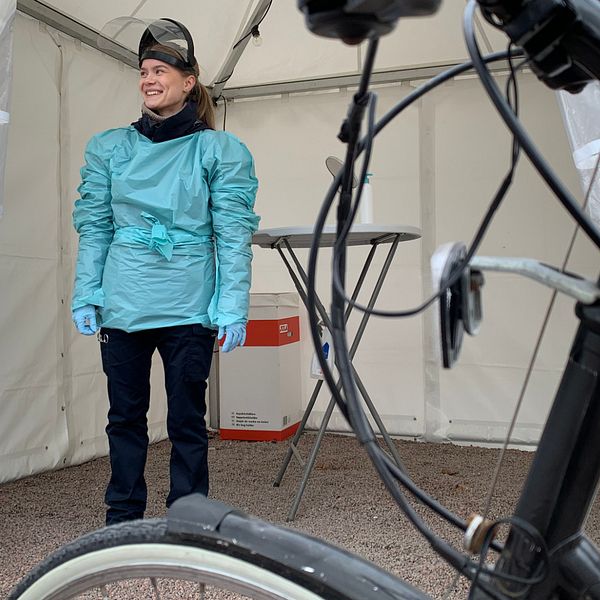 En cykel i förgrunden och en ung kvinna i ett provtagningstält i bakgrunden, hon har skyddskläder på sig.