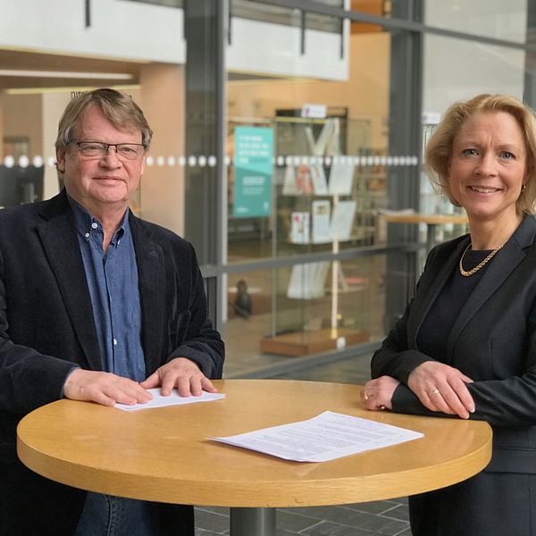 Rolf Solli och Anna Cregård vid ett ståbord framför biblioteket på Högskolan i Borås.