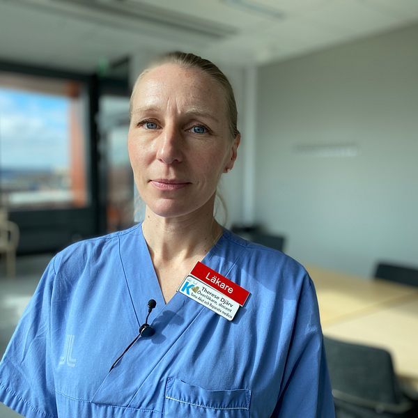 Visar forskaren och läkaren Therese Djärvi halvbild, hon har på sig blå sjukhuskläder och har håret i toffs. I kragen sitter en röd skylt där det står läkare och en vit skylt där det bland annat står att hon är överläkare och hennes namn. Bakgrunden är suddig, men man ser några fönstret och att det är i kontorsmiljö.