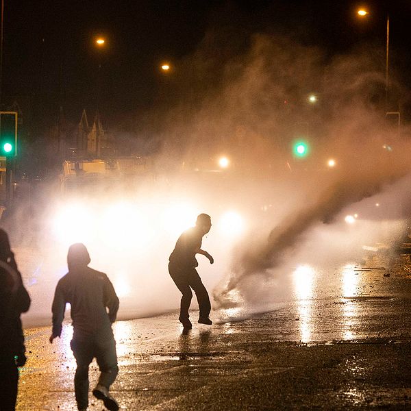 En vattenkanon skjuter en sotr stråle vatten mot svartklädda demonstranter i motljus. Våldsamheter bröt ut under torsdagen i västra Belfast när nationalistiska ungdomar attackerade polisen, som skingrade massorna med vattenkanoner.