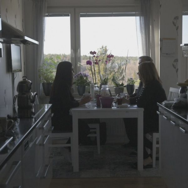 Tre personer sitter vid ett matbord i ett kök.