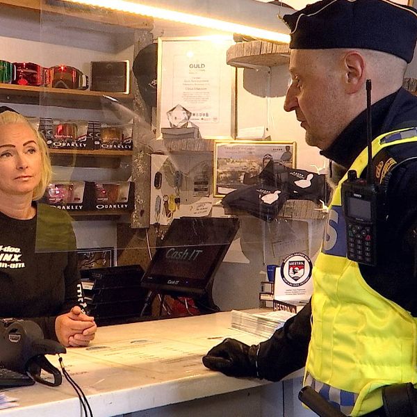en kvinna bakom den kassadisk, goggles på hyllan bakom, samt en man i poliskläder som pratar med henne