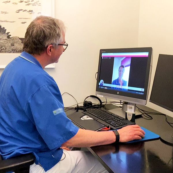 En man i blåa scrubs har ett digitalt möte framför en dator