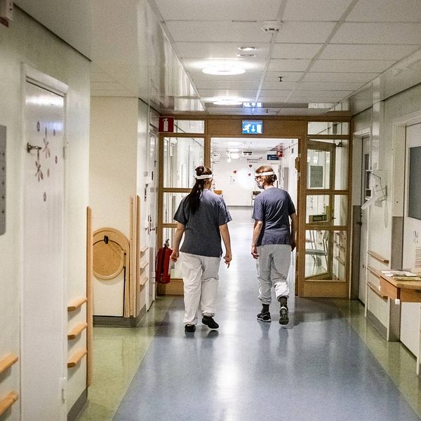 Personer i vårdkläder syns gå i en sjukhuskorridor.