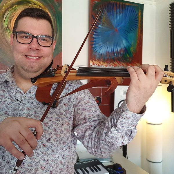 Stefan lindström håller en fiol i händerna. Han har glasögon och mörkt hår, fiolen är en el-fiol.