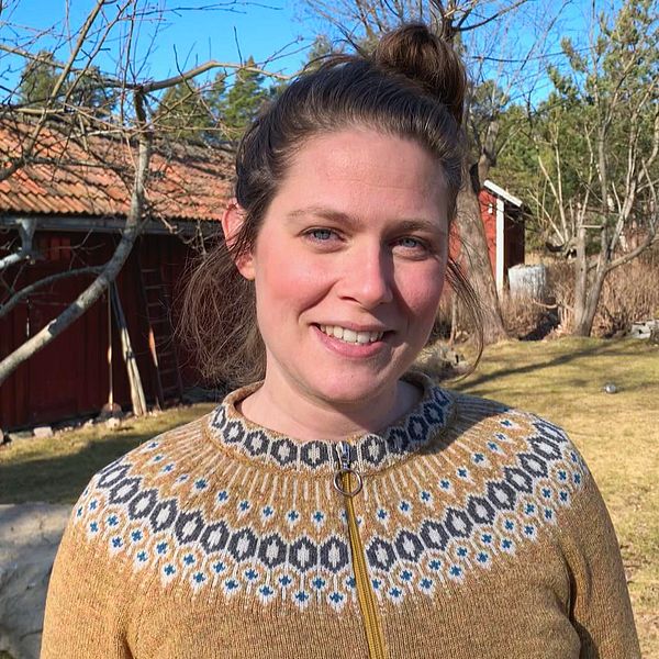 en leende kvinna i stickad tröja på en gård med trähus