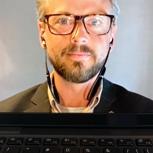 en man i kavaj, med glasögon och headset, syns på en datorskärm under en videointervju