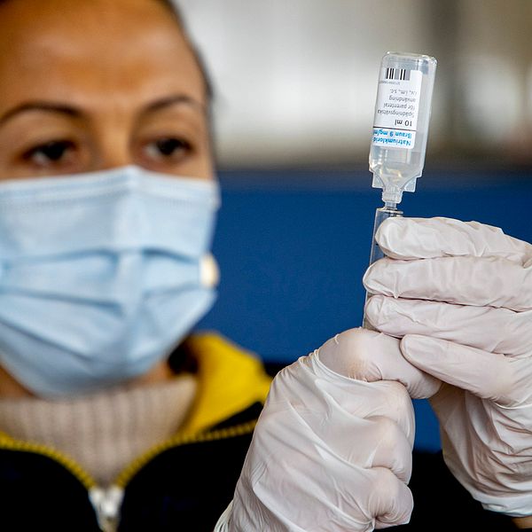 En kvinna med munskydd och handskar håller i vaccin.