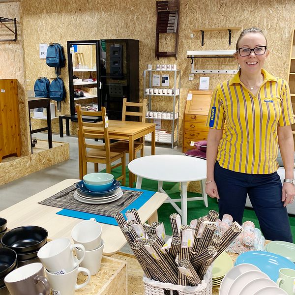 Camilla Johansson står bland en massa Ikea-möbler, iklädd gul pikétröja och glasögon. Hon ser glad ut.