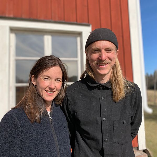 Matilda och Micke står längs med det röda huset med vita knutar och ler i solen.