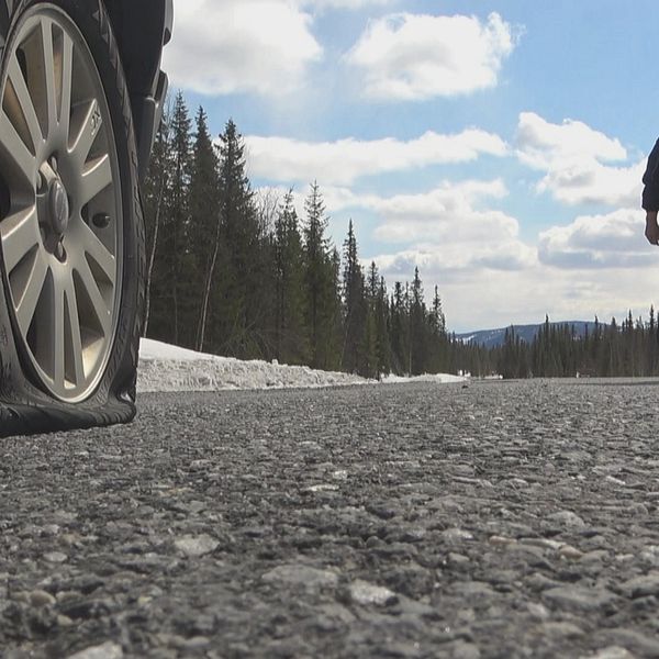 närbild på punkterat däck på en bil längs vägen, en person går i bakgrunden från en annan bil