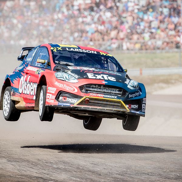 En rallycrossbil som hoppar och i bakgrunden syns ett stort publikhav.