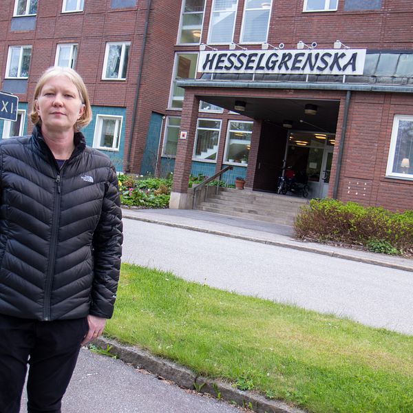 en kvinna står på gatan utanför en stor tegelbyggnad med skylten ”Hesselgrenska”