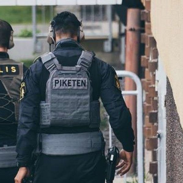 Två poliser sedda bakifrån vid ett ingripande i Vårberg i maj 2021.