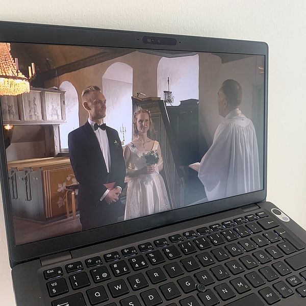 På en datorskärm syns en brudgum och brud i en kyrka framför en präst.