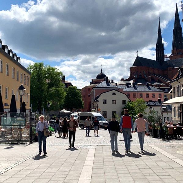 Personer går eller sitter vid uteserveringar på Gamla torget i Uppsala.