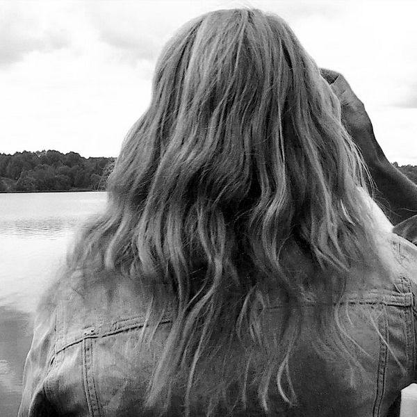 En kvinna står med ryggen vänd mot kameran och tittar ut över en sjö.