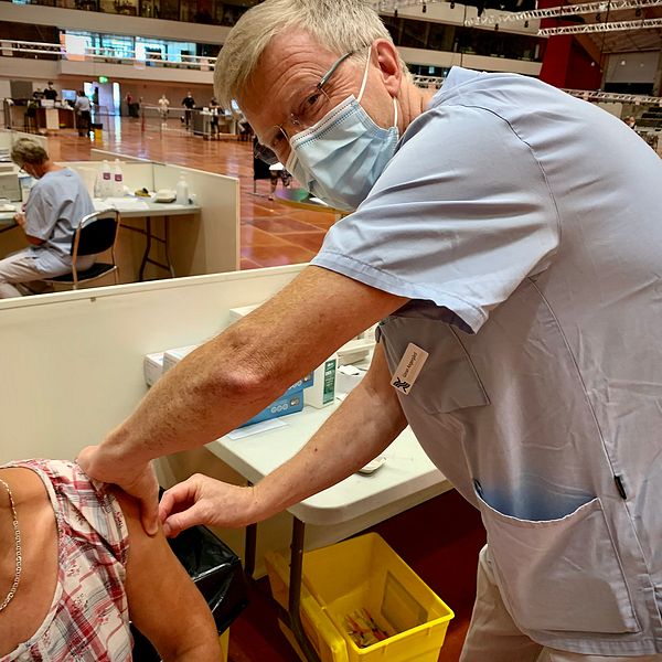 en man i sjukvårdens skorta som vaccinerar en person i en stor hall