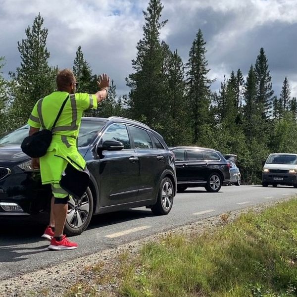 En parkeringsvakt håller upp handen och ber bilar vänta.