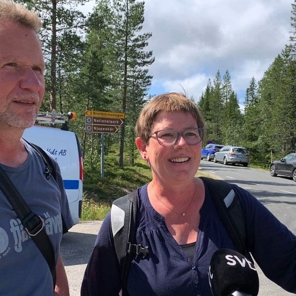 Två personer står vid Fulufjällets nationalpark. I bakgrunden ser man mängder av bilar parkerade.