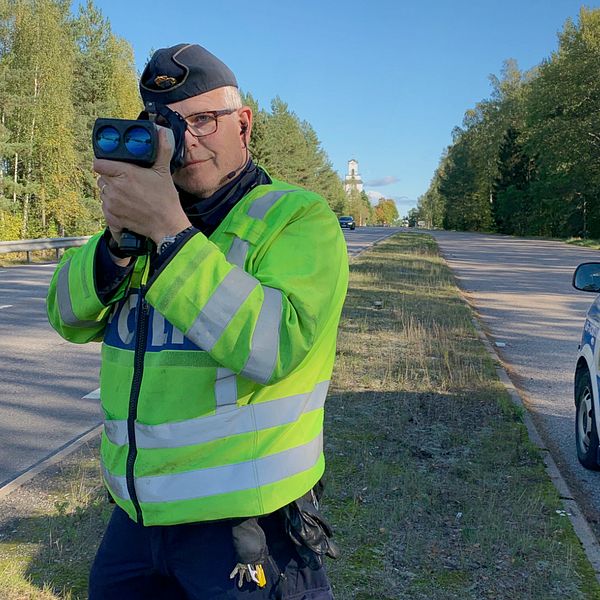 Trafikpolisen Lars Österberg som står bredvid en polisbil och skjuter med laserkikare på förbipasserande bilar.