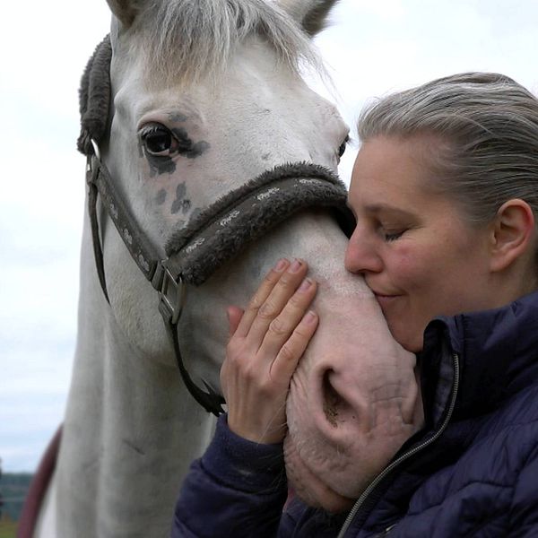 en medelålders kvinna gosar med en vit häst i hagen