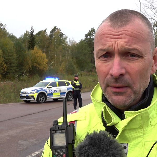 närbild på man i gul räddningsuniform med polisbil och räddningsfordon i bakgrunden