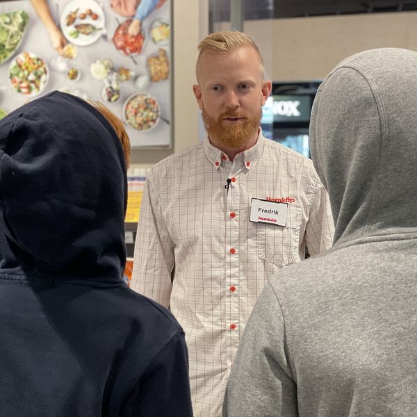En man med skägg pratar med två ungdomar i en butik.