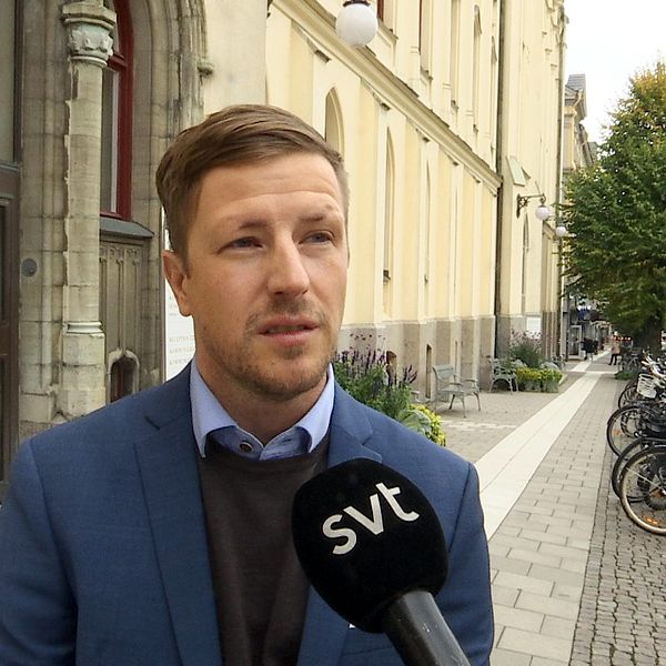 På bilden står Jimmy Nordengren utanför Rådhuset i Örebro, Han är klädd i blå kostym med en svart tröja under och en blå skjorta som sticker fram under kragen.