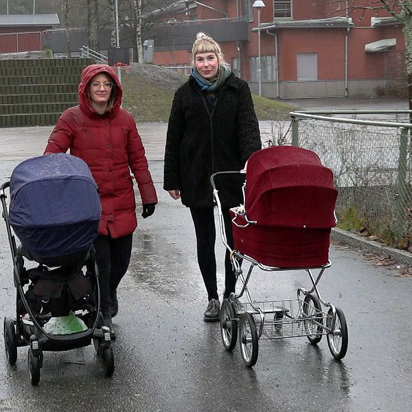 Två kvinnor med varsin barnvagn står på en regnig asfaltsyta.