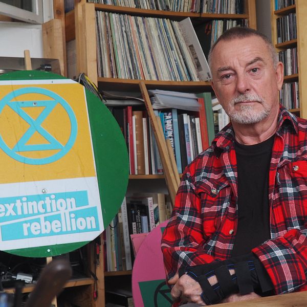 En man i rutig skjorta bredvid en skylt med miljöaktivistgruppen Extinction Rebellions namn
