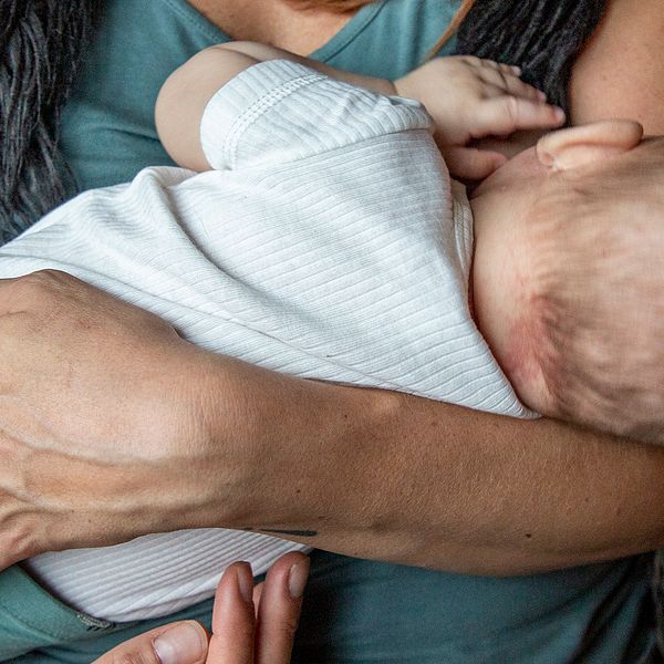 närbild på kvinna som håller ett spädbarn och ammar, ansiktena syns inte