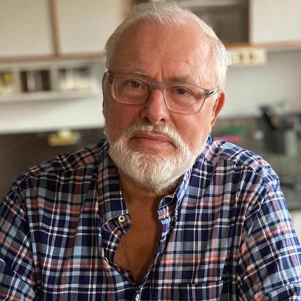 En bild på Staffan Lagerström som sitter i sitt kök. Han är en man i 75-årsåldern med vitt hår och vitt skägg.