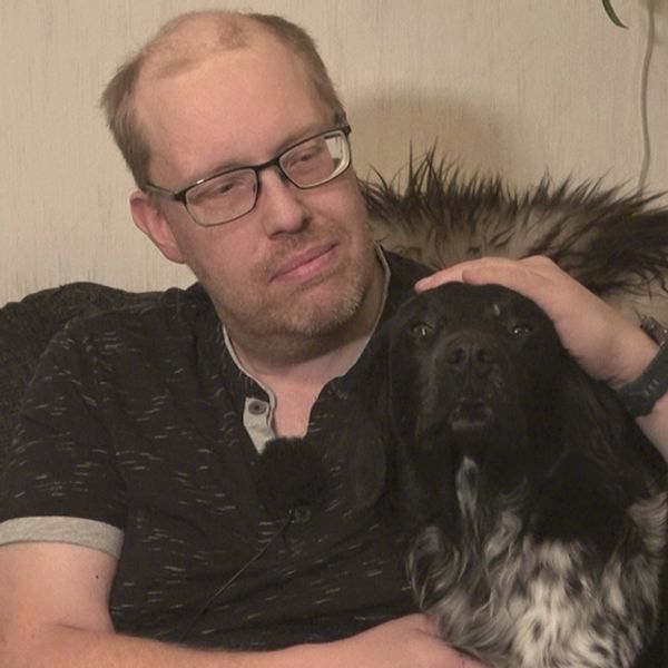 En man sitter i en soffa och stryker en hund över huvudet.