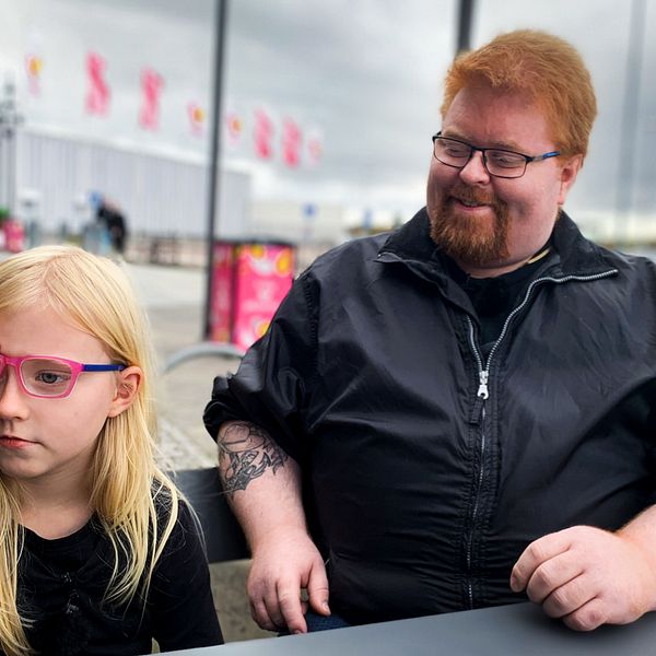 Två personer sitter vid ett bord utomhus nära en byggnad med färgglada flaggor i bakgrunden.