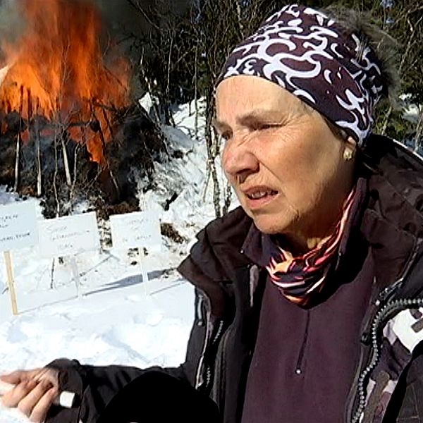 En äldre kvinna står framför en kåta som brinner