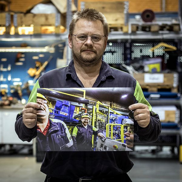 en man i verkstadsmiljö håller upp en bild på skrattande människor i verkstadsmiljö
