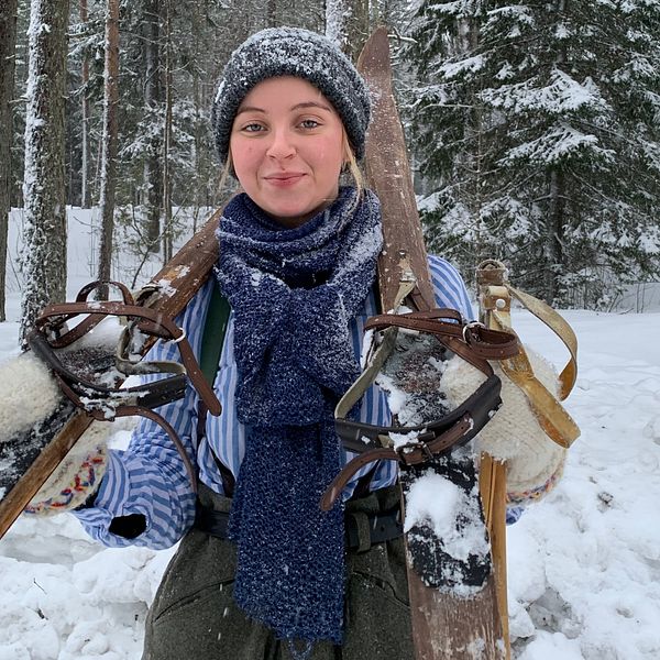 En kvinna med snöiga kläder håller i gammal skidutrustnung.