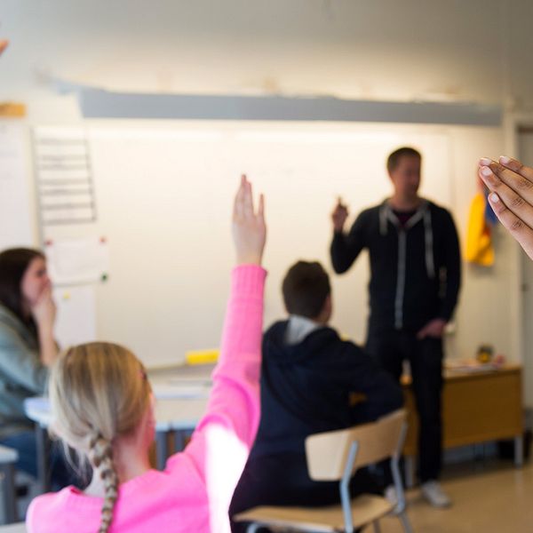 Elever räcker upp handen i ett klassrum.