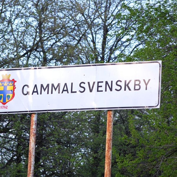 Skylt med texten ”Gammalsvenskby” i grönskande omgivning.