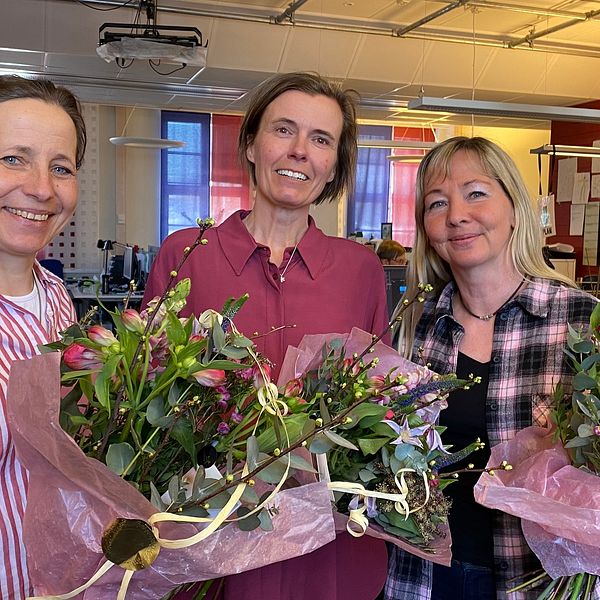 Tre kvinnor står bredvid varandra med blomkvastar. De är glada.